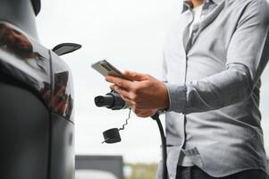 hombre participación poder cargando cable para eléctrico coche en al aire libre coche parque foto