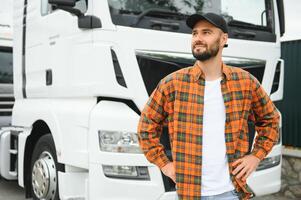 Portrait of young bearded man standing by his truck. Professional truck driver standing by semi truck vehicle. photo