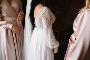 Bridesmaid preparing bride for wedding day. Bridesmaid helping bride fasten lacing her wedding white dress before ceremony. Luxury bridal dress close up. Wedding morning moments details concept. photo