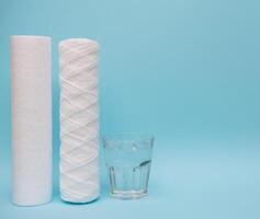 Water filters. Carbon cartridges and a glass with water on a blue background. Household filtration system photo