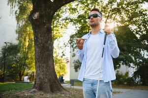 Young blind man with smartphone in city, calling photo