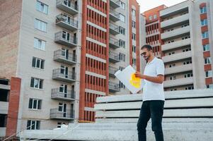 Portrait of an architect builder studying layout plan of the rooms, serious civil engineer working with documents on construction site. photo