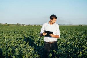 Agronomist holds tablet touch pad computer in the soy field and examining crops before harvesting. Agribusiness concept. agricultural engineer standing in a soy field with a tablet in summer. photo