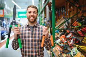 un cliente elige un jardín tijeras para él mismo en un jardín suministro Tienda foto