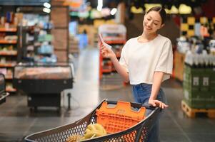 Woman at supermarket holding a full shopping cart and a shopping list photo