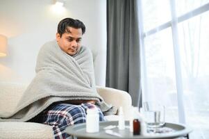 enfermo indio hombre en tartán sentar solo temblando desde frío. insalubre árabe chico sentar en silla sensación incomodidad tratar a calentamiento arriba foto