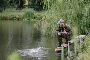 pescar en rio.a pescador con un pescar varilla en el río banco. hombre pescador capturas un pescado pesca del lucio, hilado carrete, pez, breg ríos - el concepto de un rural escapar. artículo acerca de pescar foto