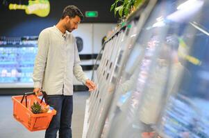 Portrait of handsome young Indian man standing at grocery shop or supermarket, Closeup. Selective Focus. photo