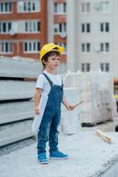 arquitecto en casco escritura alguna cosa cerca nuevo edificio. pequeño linda chico en el edificio como un arquitecto foto