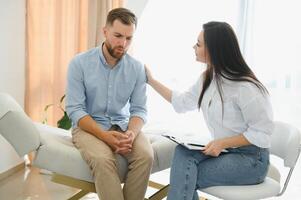 Depressed man speaking to a therapist while she is taking notes photo