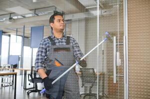 Male janitor cleaning window in office photo