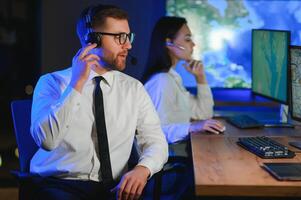 Center of dispatching maintenance. Portrait of cheerful woman and man working via headset microphone while sitting on navigation controller board photo