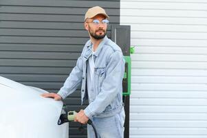 Stylish man inserts plug into the electric car charging socket photo