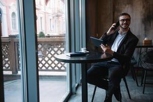 Young businessman talking on mobile phone while working on tablet in cafe. photo