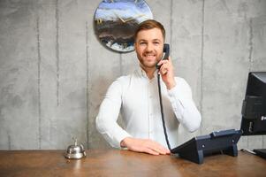 retrato de un joven masculino recepcionista en un hotel vestíbulo vistiendo un blanco camisa foto