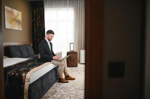 retrato de contento empresario sentado con ordenador portátil en cama en hotel habitación foto