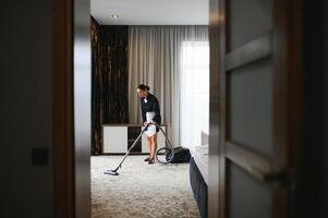 Young Housekeeper Cleaning Carpet With Vacuum Cleaner In Hotel Room photo