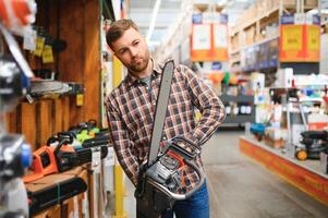 joven masculino es en pie con nuevo eléctrico Sierra en herramientas Tienda foto