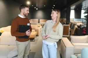 joven vendedor Ayudar cliente a escoger nuevo moderno sofá en Tienda foto