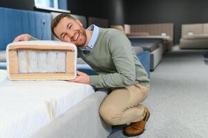 Handsome man examining sample of orthopedic mattress on sale photo