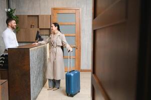 hembra invitados ven con pantalones y maletas a el hotel recepción en el vestíbulo foto