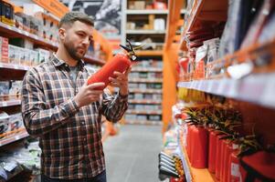 un hombre sostiene un fuego extintor en su mano. un comprador en un hardware Tienda selecciona un producto foto