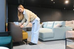 contento joven mujer elige sofá para hogar en mueble Tienda foto