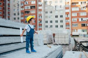 arquitecto en casco escritura alguna cosa cerca nuevo edificio. pequeño linda chico en el edificio como un arquitecto foto