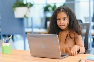 African american girl sitting at table, using laptop for online lesson photo