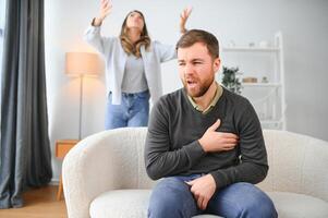 Couple arguing. Wife shouting to her desperate husband sitting on a couch in the living room at home photo