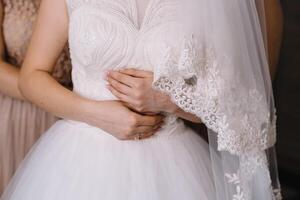 dama de honor preparando novia. dama de honor ayuda sujetar un Boda vestir el novia antes de el ceremonia. lujo nupcial vestir cerca arriba. mejor Boda Mañana foto