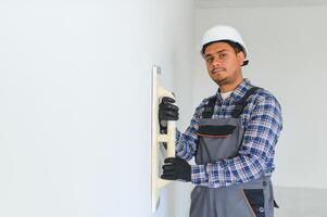 un indio trabajador trabajos en un vacío departamento. un hombre en un uniforme hace refacción dentro el edificio foto