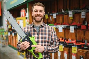 joven masculino es en pie con nuevo eléctrico Sierra en herramientas Tienda foto