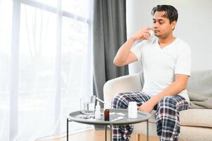 rhinitis, medicine and healthcare concept - sick indian man in blanket using nasal spray at home photo