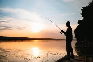 Fisher man fishing with spinning rod on a river bank at misty foggy sunrise. fisher with spinning. spinning concept. photo