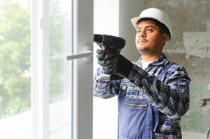 indio obrero en mono instalando o ajustando el plastico ventanas en el vivo habitación a hogar foto