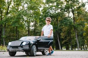 Cute boy in riding a black electric car in the park. Funny boy rides on a toy electric car. Copy space. photo