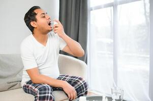 un indio hombre tiene el gripe. un hombre usos un garganta rociar. foto