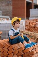 arquitecto en casco escritura alguna cosa cerca nuevo edificio. pequeño linda chico en el edificio como un arquitecto foto