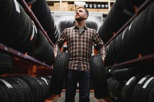 Male mechanic holding car tire in automobile store photo