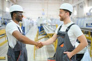 Two Diverse Professional Heavy Industry Engineers Wearing Safety Uniform and Hard Hats Working on Laptop photo