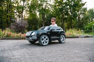 Cute boy in riding a black electric car in the park. Funny boy rides on a toy electric car. Copy space. photo