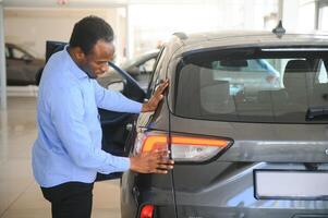 su sueño coche. contento joven africano hombre mirando emocionado elegir un coche a el concesión foto