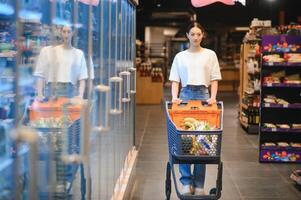 Smiling happy woman enjoying shopping at the supermarket, she is leaning on a full cart photo