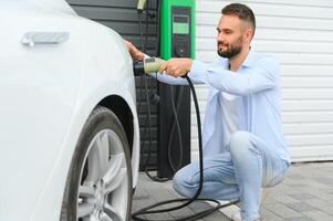 elegante hombre inserta enchufe dentro el eléctrico coche cargando enchufe foto