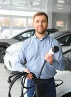 A happy man chooses a new electric car at a car dealership. The concept of buying an ecological car photo