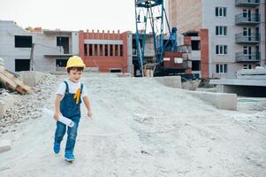 arquitecto en casco escritura alguna cosa cerca nuevo edificio. pequeño linda chico en el edificio como un arquitecto foto