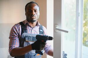 de cerca de joven africano personal de mantenimiento en uniforme instalando ventana foto