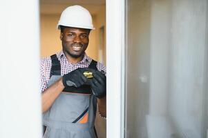 joven africano personal de mantenimiento en uniforme fijación vaso ventana con destornillador foto