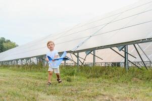 Little happy boy playing with toy airplane near solar panels. photo